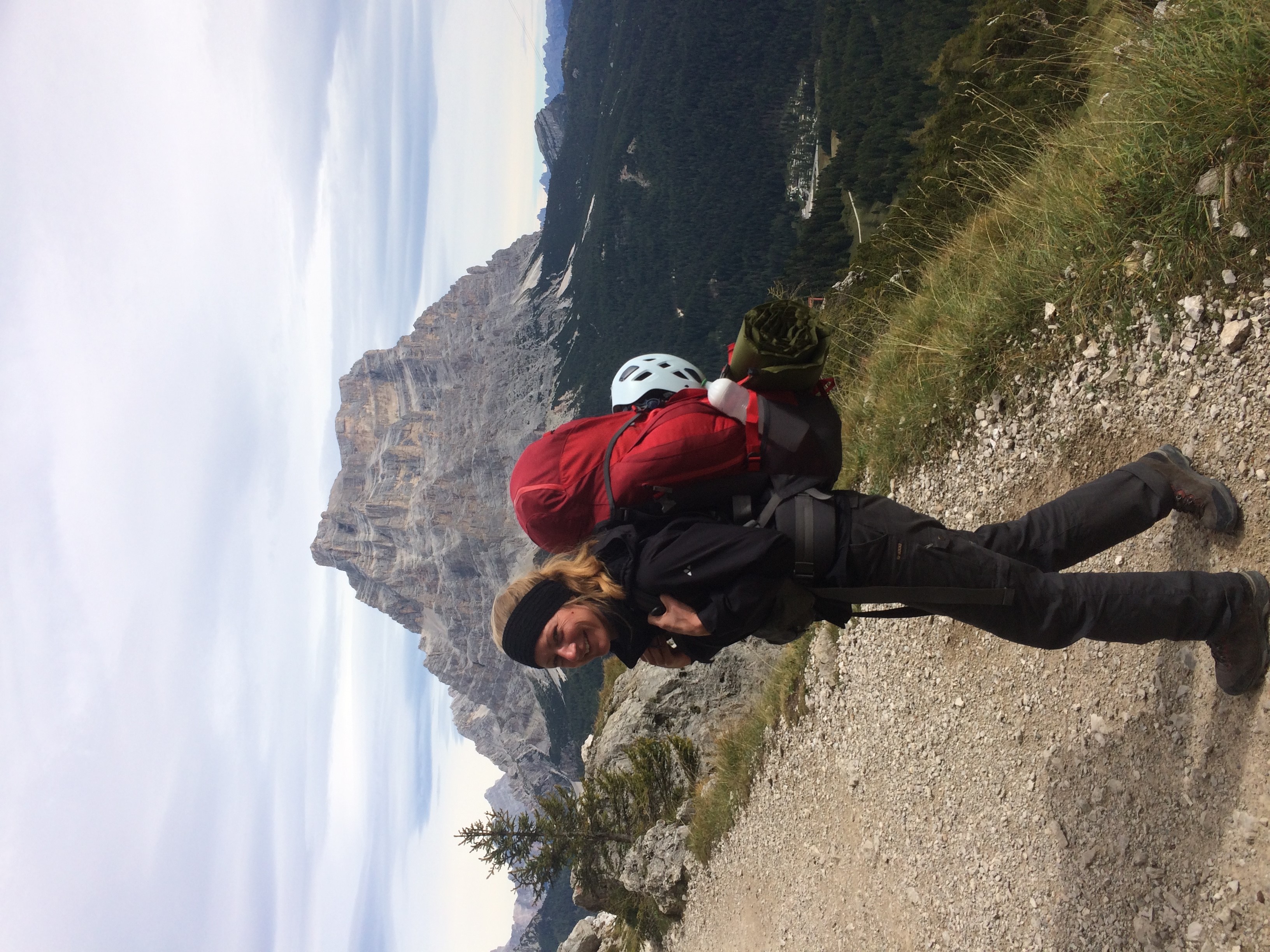 Photo of a woman in front of the dolomite mountains with a backpack on.