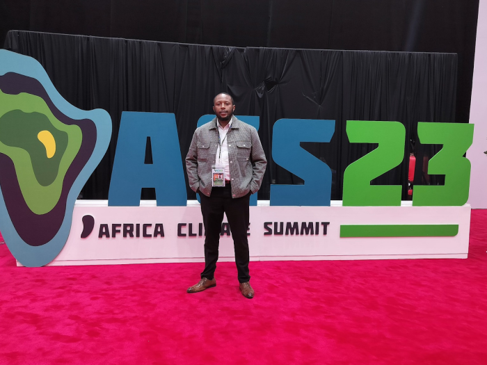 Jonathan Gichuru stands in front of the Africa Climate Summit '23 sign.