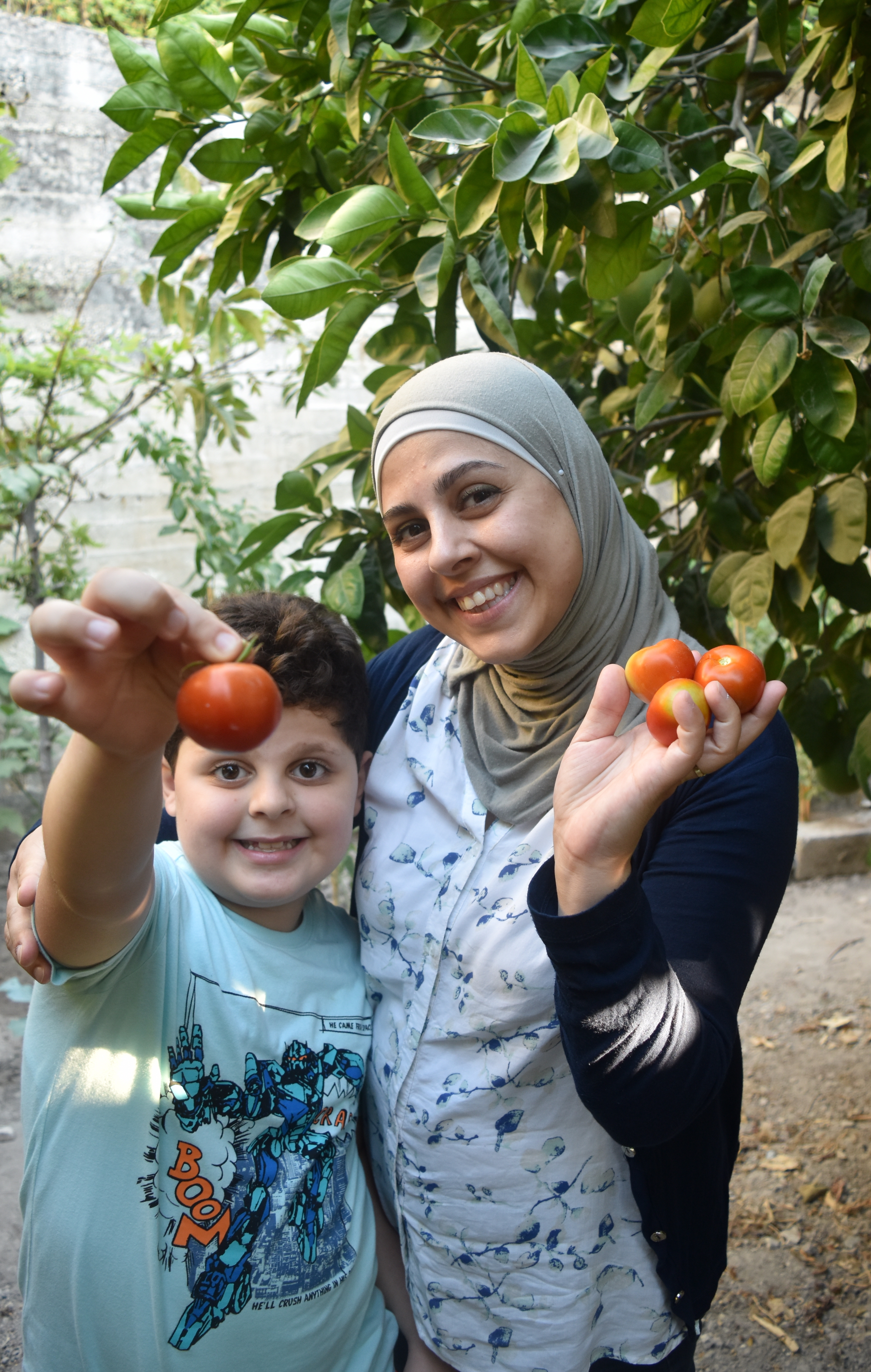 Photo of a woman and a young boy holding up tomatoes and smiling. 