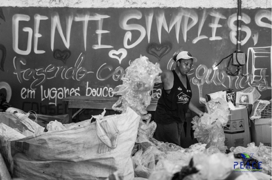Photo of a woman sorting through trash in front of a wall spray painted with different arts and phrases.
