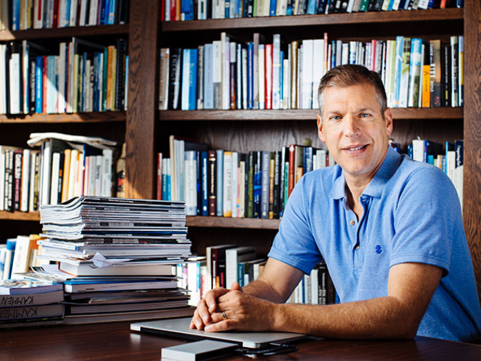 Dan Kammen sitting at his desk smiling at the camera with a bookshelf behind him