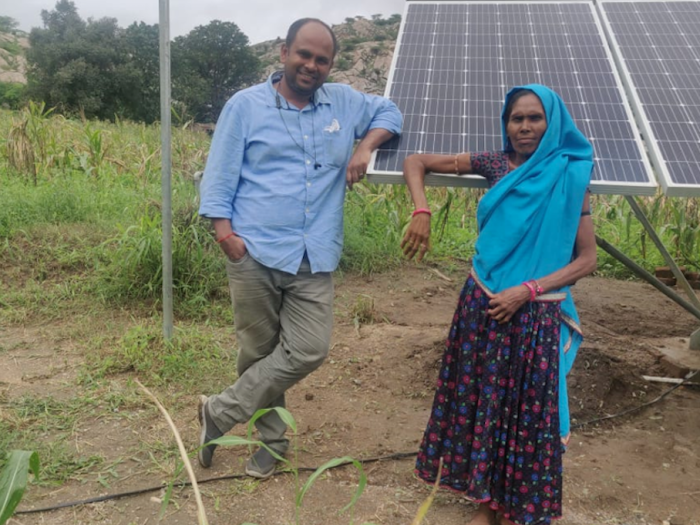 Two people smiling in front of solar panels in a field. 